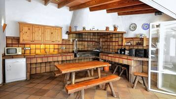 A rustic kitchen with wooden cabinets, a tiled backsplash, a wooden table, and benches.