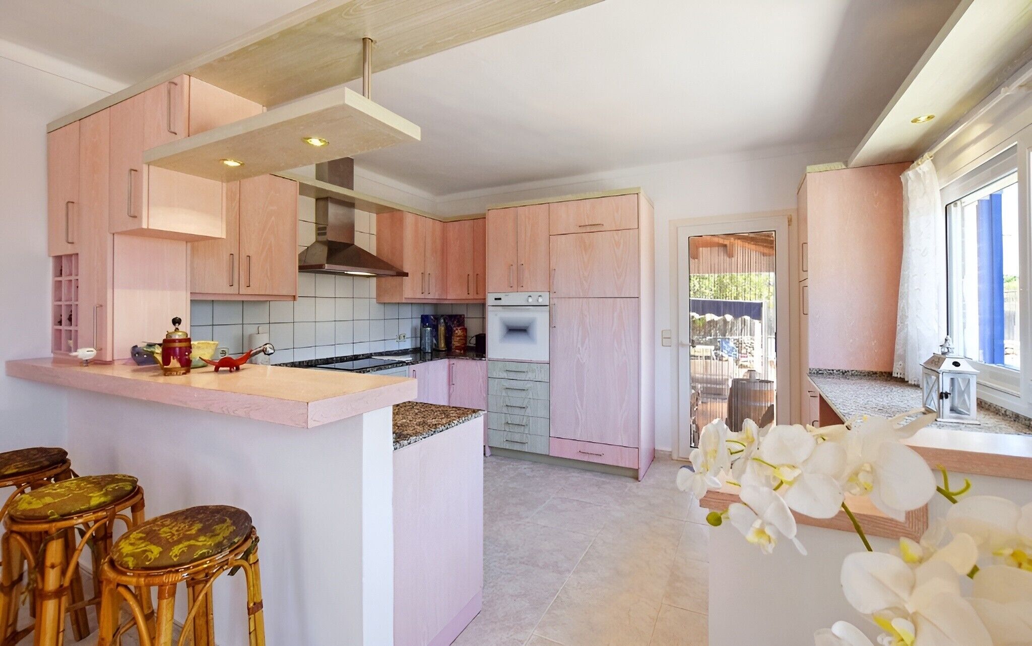 A modern kitchen with pink cabinets, a central island, and a view to the backyard.
