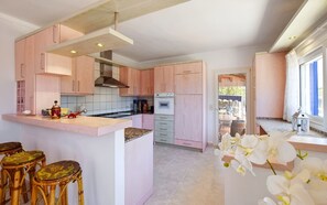 Une cuisine moderne avec des meubles roses, un îlot central et une vue sur le jardin arrière.
