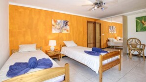 Ein Hotelzimmer mit zwei Betten, einem Deckenventilator, Bildern an den Wänden und einem Sessel.