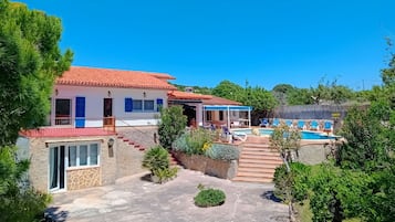 A villa with a swimming pool, a covered patio, and a stone staircase leading to the entrance.