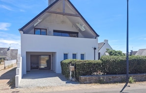 A modern two-story house with a prominent gable roof, a front entrance with a glass door, and a small garden area with a hedge. - 1 bedroom beach front apartment in Penmarc'h (Penmarc'h)