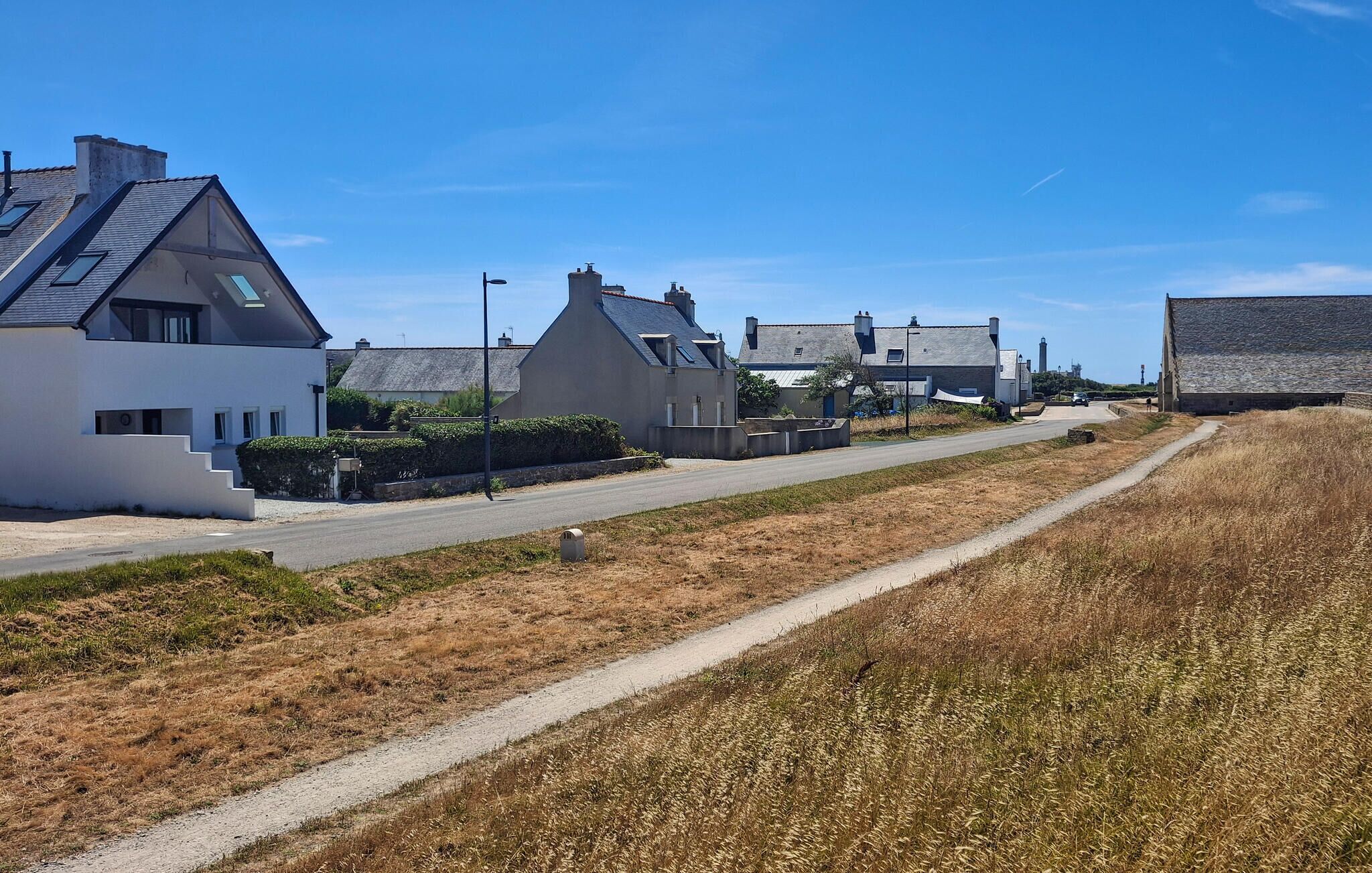 A residential street with houses, a clear sky, and a dirt path.
