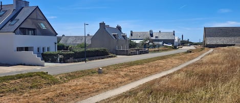 A residential street with houses, a clear sky, and a dirt path.