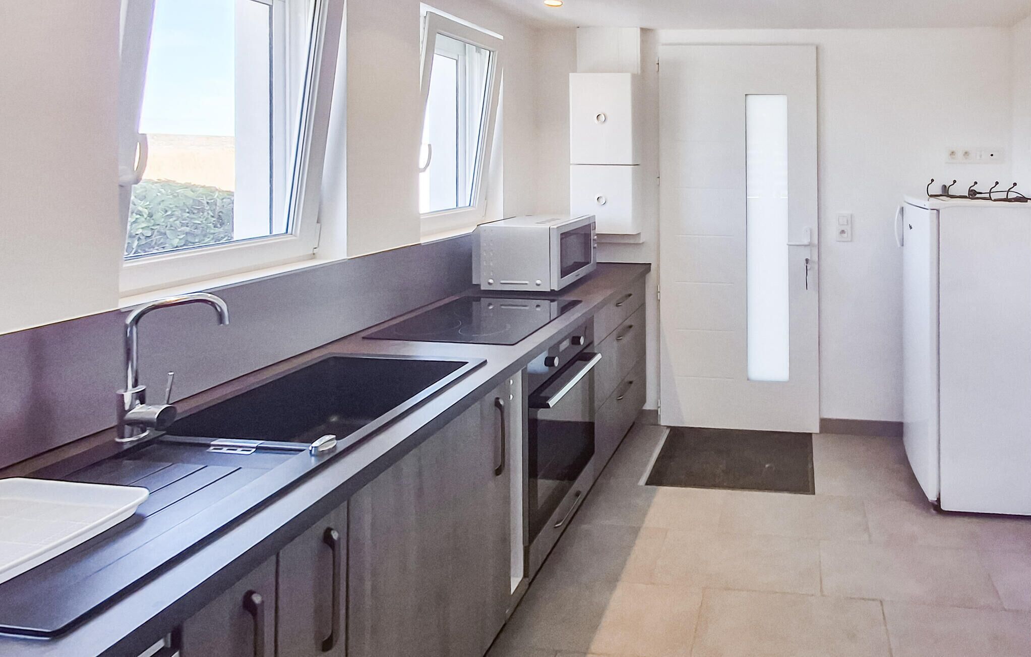 A modern kitchen with a stainless steel sink, a microwave, and a refrigerator.