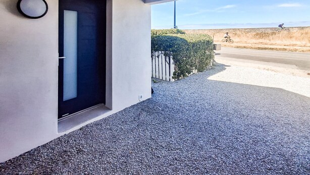 Entrada de un edificio moderno con camino de grava, una puerta y vista de un ciclista en la carretera.