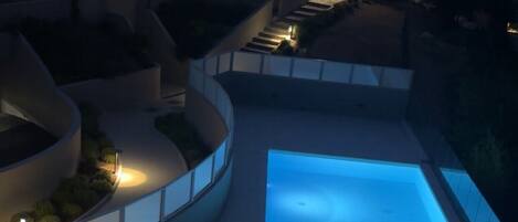 A swimming pool with a curved deck, surrounded by a low wall and a fence.