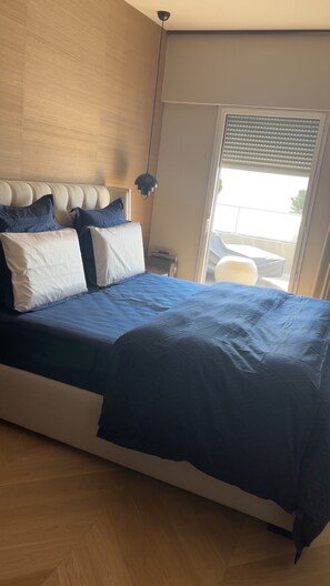 Un dormitorio con cama, mesita de noche, lámpara y vistas al exterior a través de una ventana.