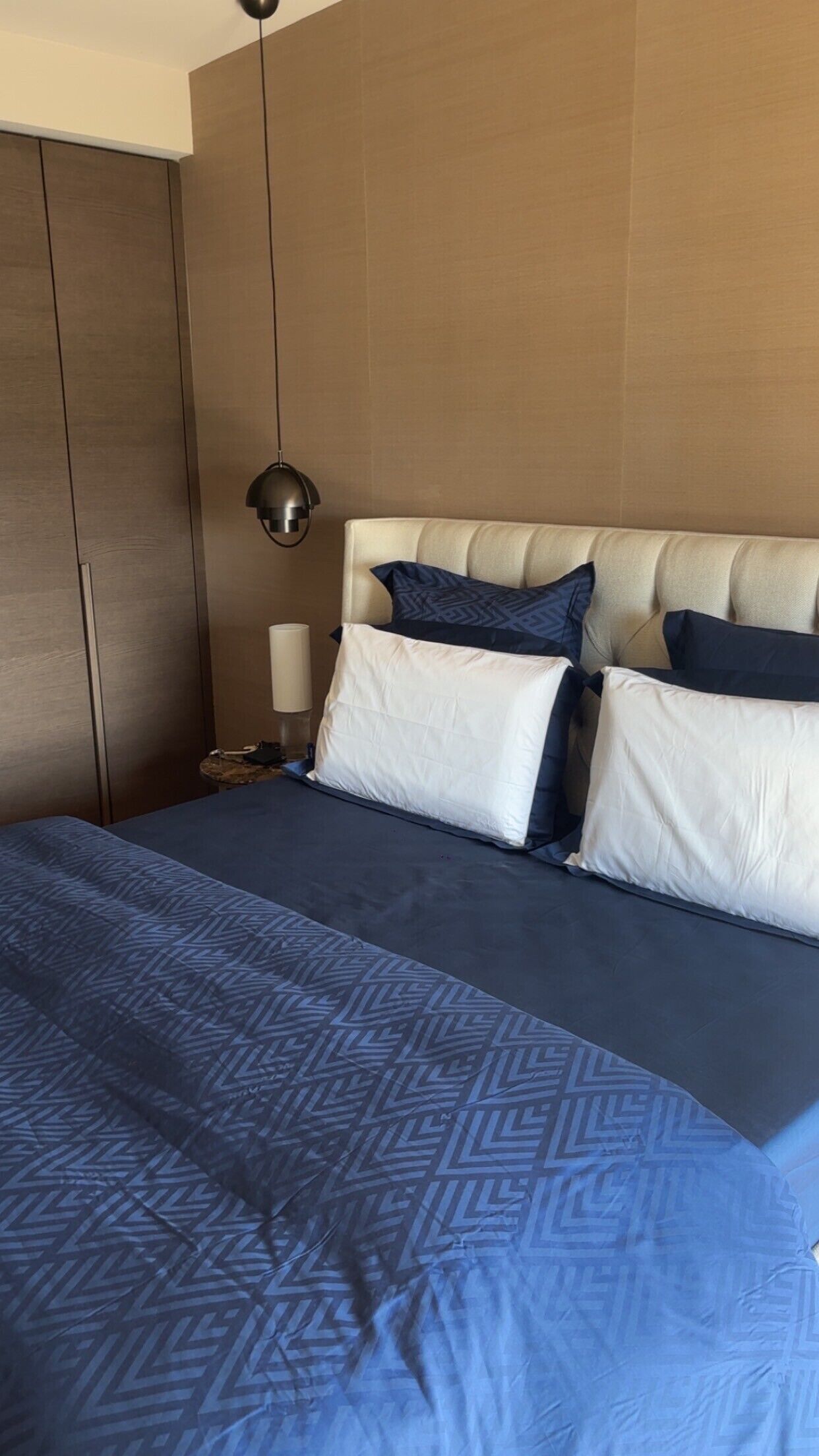 Een hotelkamer met een bed, nachtkastje, lamp en kledingkast.