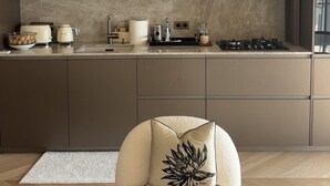 A modern kitchen with built-in appliances, a round chair with a decorative pillow, and a herringbone-patterned floor. - Luxury Apartment in Nice – Sea and Mountain Views, Near Monaco (Nice)