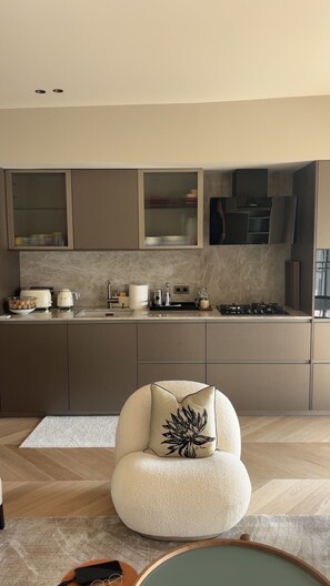 A modern kitchen with built-in appliances, a round chair with a decorative pillow, and a herringbone-patterned floor. - Luxury Apartment in Nice – Sea and Mountain Views, Near Monaco (Nice)