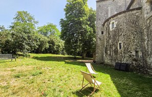 Ein Steinhaus mit einem Rasen, einer Bank und einem Klappstuhl.
