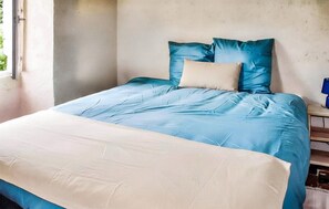 Een bed met een blauw-witte dekbedovertrek, een beige kussen en een houten nachtkastje met een lamp.