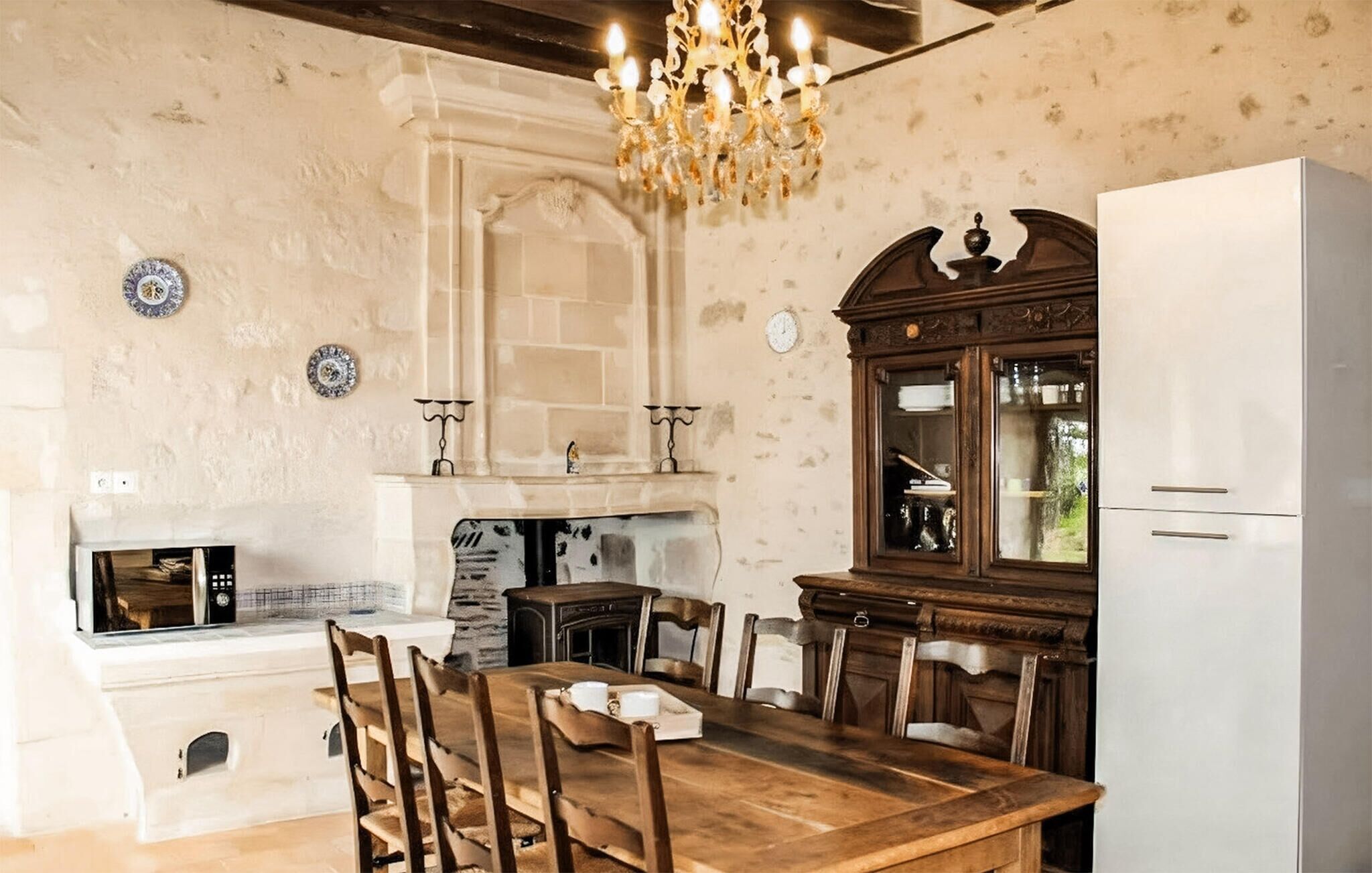 Een eetruimte met een houten tafel, stoelen, een kroonluchter, een koelkast en een klok aan de muur.