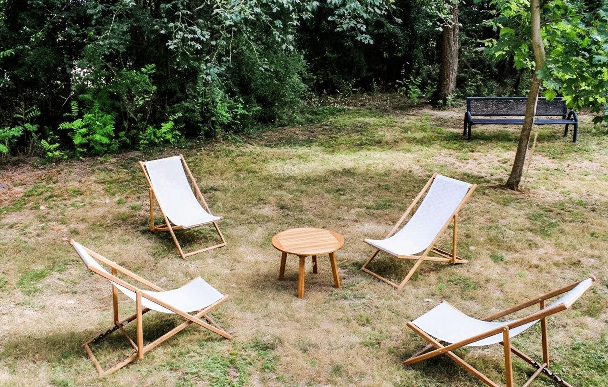 Un espace extérieur aménagé avec quatre fauteuils en bois et une petite table ronde, le tout entouré de pelouse et d’arbres.