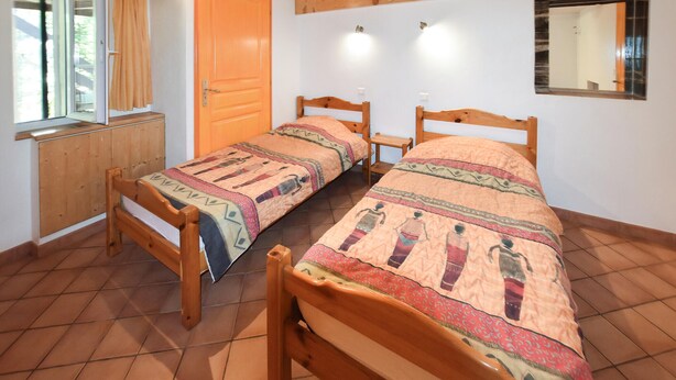 Une pièce avec deux lits en bois, une armoire en bois, une fenêtre avec des rideaux et un miroir au mur.