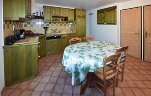Eine kleine Küche mit Holzausstattung, einem Esstisch mit Stühlen und Fliesenboden.