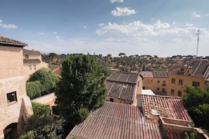 A view of a town with terracotta-roofed buildings, a prominent tree, and a clear sky.