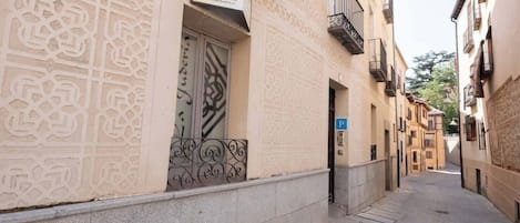 A narrow street with a building featuring intricate facade patterns, a visible door, and a blue parking sign.