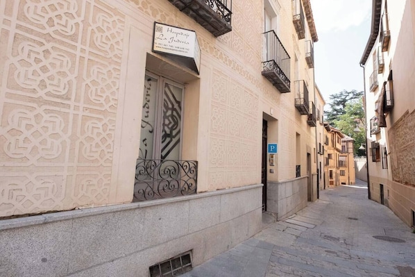 A narrow street with a building featuring intricate facade patterns, a visible door, and a blue parking sign.