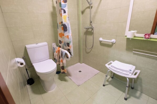 A bathroom with a toilet, shower, and a small sink area with a towel rack.