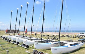 A row of sailboats parked on a grassy area near a beach.
