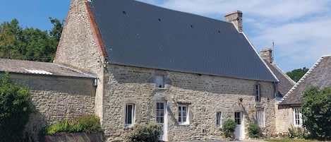 Un edificio de piedra con techo inclinado, camino de grava y un pequeño jardín.