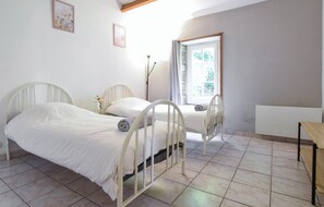 Une chambre avec deux lits, une fenêtre avec des rideaux, un radiateur et une petite table.
