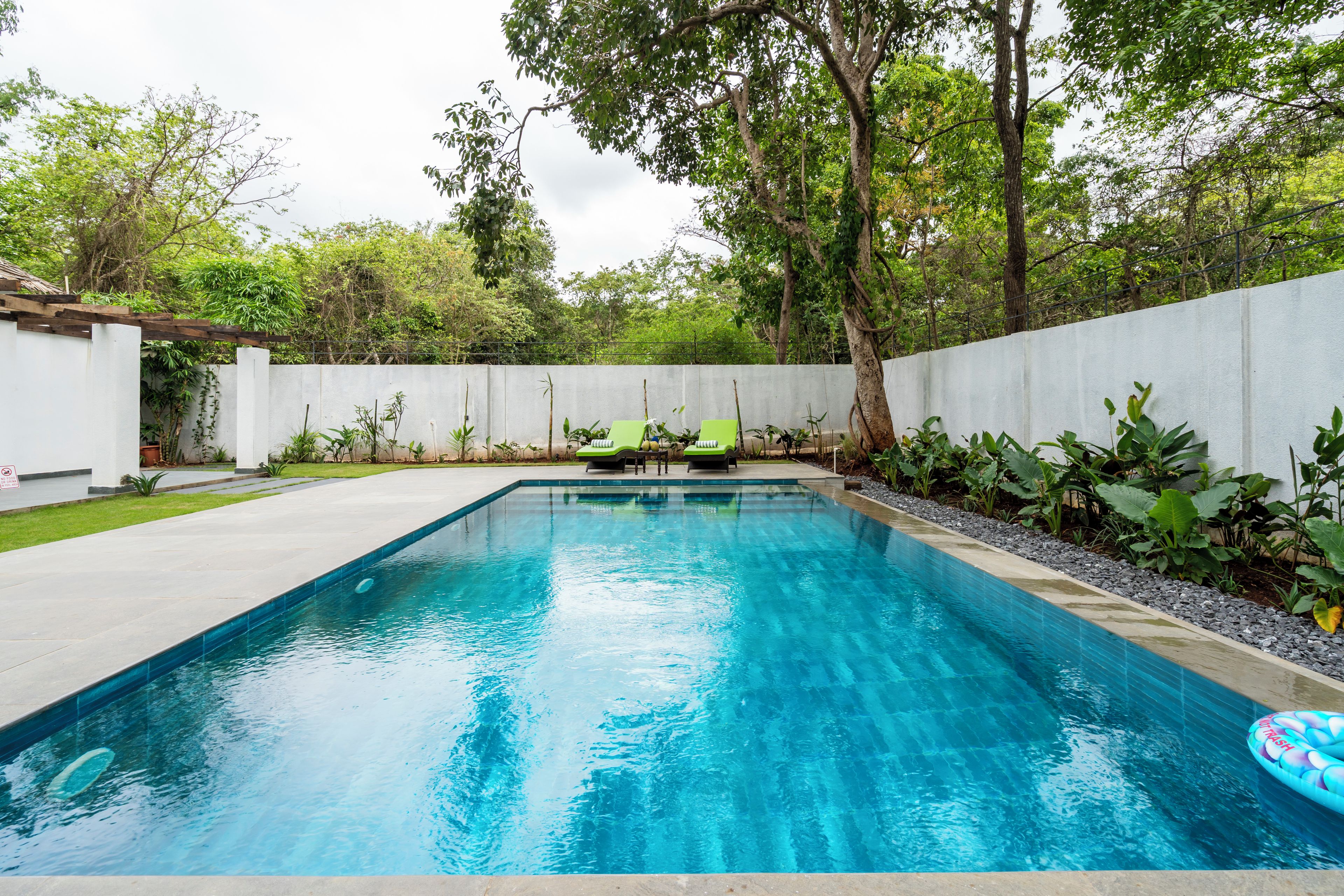 A rectangular swimming pool with clear blue water, surrounded by a concrete deck and a low white wall.