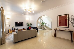 A modern living room with a flat-screen TV, a sofa, a guitar, and a staircase leading to an upper level.