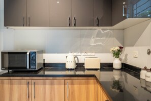 Eine moderne Küche mit Mikrowelle, Toaster und Wasserkocher auf der Arbeitsfläche, Holzschränken darunter und einer Vase mit Blumen an der Wand.