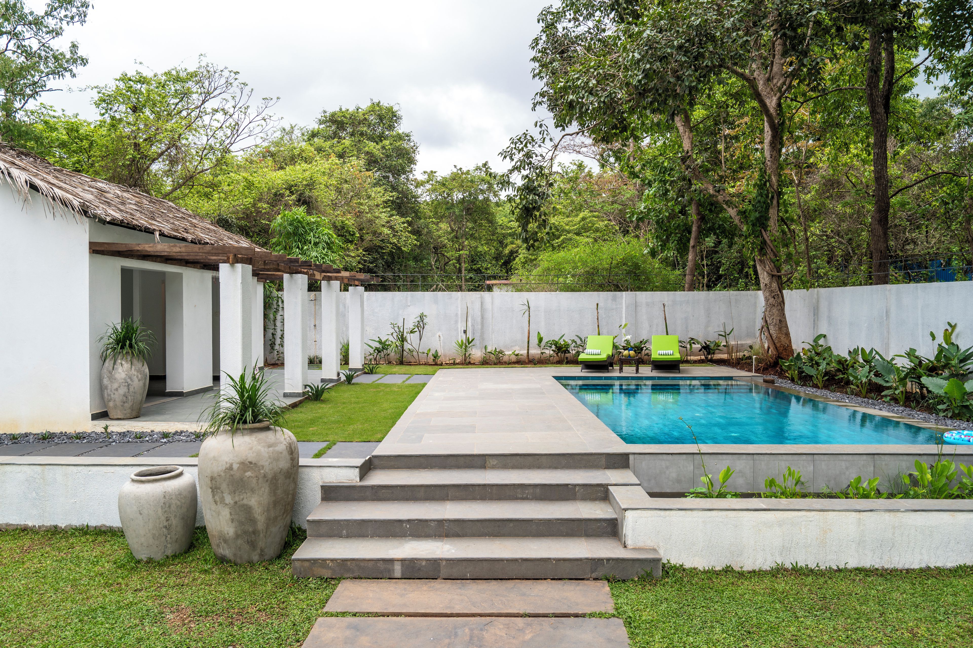 A swimming pool with steps leading to it, surrounded by a white fence, with greenery and trees in the background.