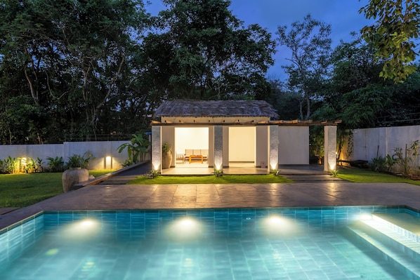 A poolside area with a covered seating area, a pool, and surrounding greenery. - Staymaster Caetano-3BR Villa with Pool  (Siolim)