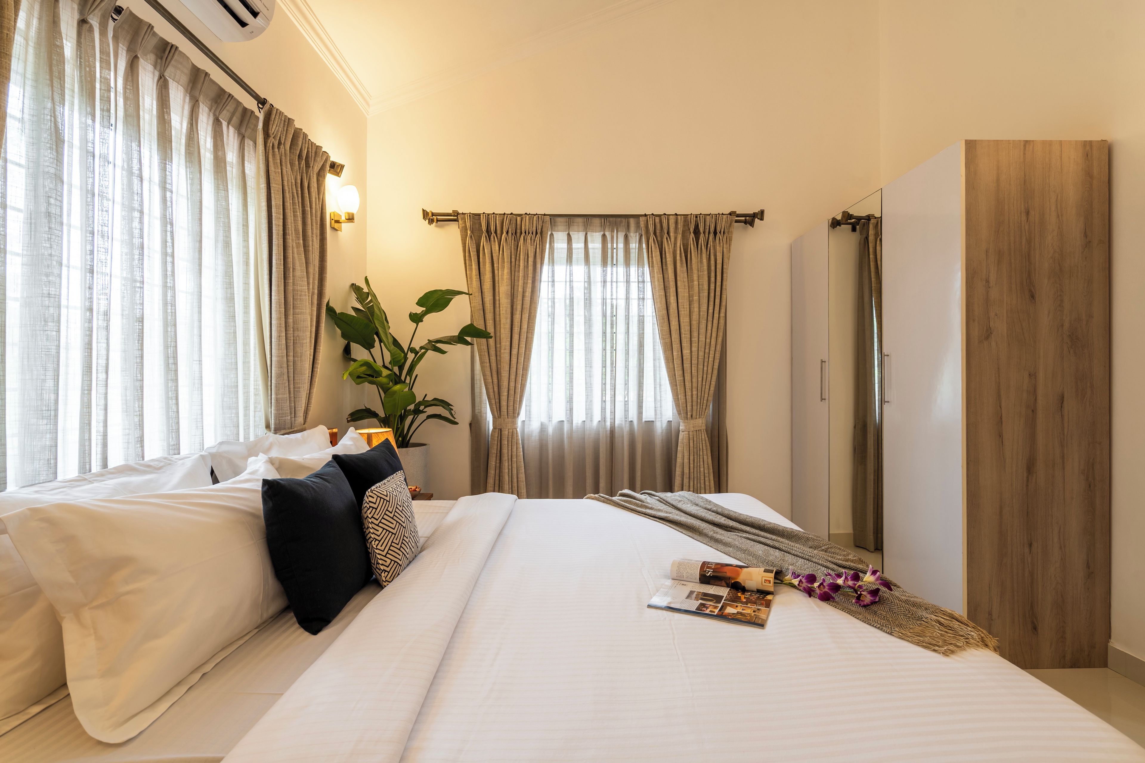 Une chambre d’hôtel avec un grand lit, une table de chevet avec une lampe, une plante en pot et une armoire en bois.