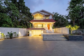 A two-story house with a balcony, a staircase leading to the entrance, and a driveway. - Staymaster Caetano-3BR Villa with Pool  (Siolim)