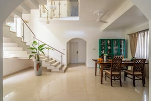 A spacious interior with a staircase, a dining area, and a green cabinet with decorative items. - Staymaster Caetano-3BR Villa with Pool  (Siolim)