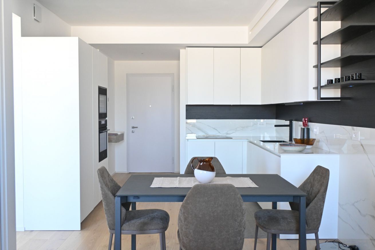A modern kitchen with white cabinetry, a marble countertop, and a dining area with a table and chairs.