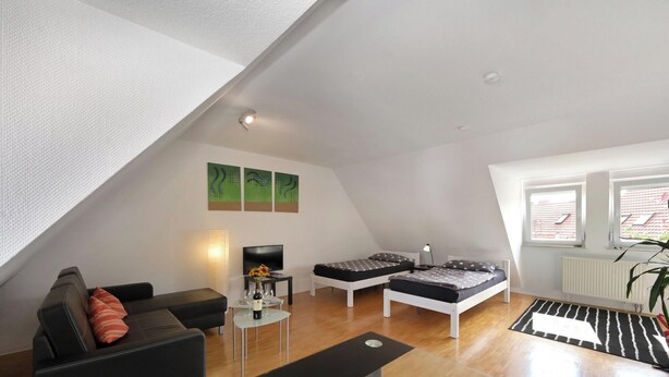 Habitación estilo loft con techo inclinado, un sofá, una pequeña mesa con un florero, dos camas con ropa de cama de estampado de estrellas y un radiador.