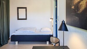 Una camera da letto con un letto, una sedia, una scrivania, una lampada, un quadro e una tenda.