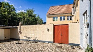 Un cortile con pavimento in pietra, un cancello rosso e un edificio con tetto in tegole.