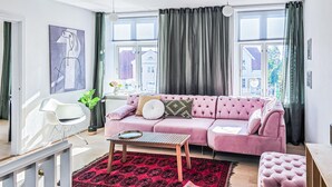 Un soggiorno moderno con un divano rosa, un tavolino in legno, un tappeto rosso con motivo e una sedia bianca.