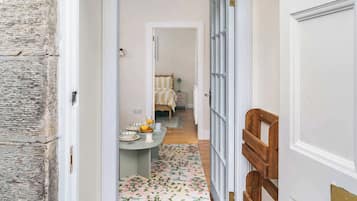 A hallway leading to a dining area with a table set for two, a bed in the background, and a wooden bench.