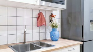 Eine Küche mit einem Edelstahl-Spülbecken, einer blauen Vase mit Blumen und einem rot-weißen karierten Handtuch an der Wand.