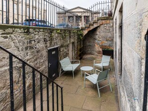 A stone-walled courtyard with a metal staircase, a black door, and outdoor seating. - Charming 1BR in Edinburgh Old Town (Edinburgh)