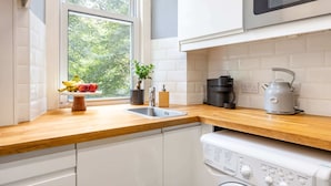 A modern kitchen with white cabinets, a wooden countertop, a stainless steel sink, a coffee maker, and a kettle. - Stylish 2BR Walk to Edinburgh Castle (Edinburgh)