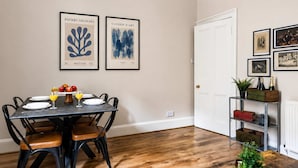 A dining area with a table set for four, framed artwork on the wall, and a door leading to another room. - Stylish 2BR Walk to Edinburgh Castle (Edinburgh)
