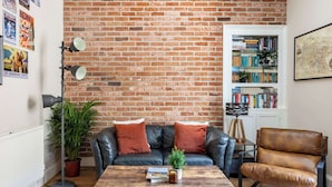 A living room with a brick wall, a leather sofa, a coffee table with books, a bookshelf, and a potted plant. - Stylish 2BR Walk to Edinburgh Castle (Edinburgh)