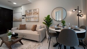 A modern living room with a sofa, coffee table, dining table set for four, and a large mirror. - Modern 1BR w/ Balcony | Maryah Vista Retreat (Abu Dhabi)