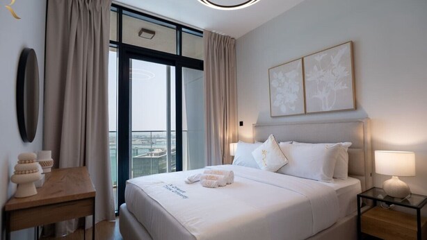 A modern hotel room with a large bed, a bedside table, a nightstand, and a view of the city. - Modern 1BR w/ Balcony | Maryah Vista Retreat (Abu Dhabi)