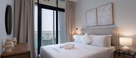 A modern hotel room with a large bed, a bedside table, a nightstand, and a view of the city.